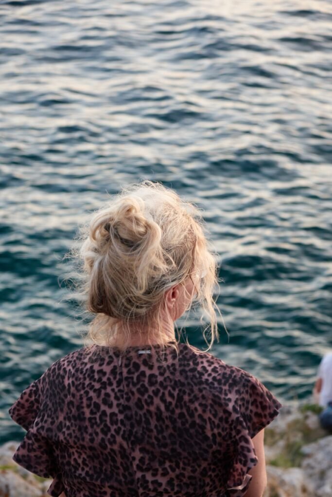 a woman sitting on a rock next to a body of water