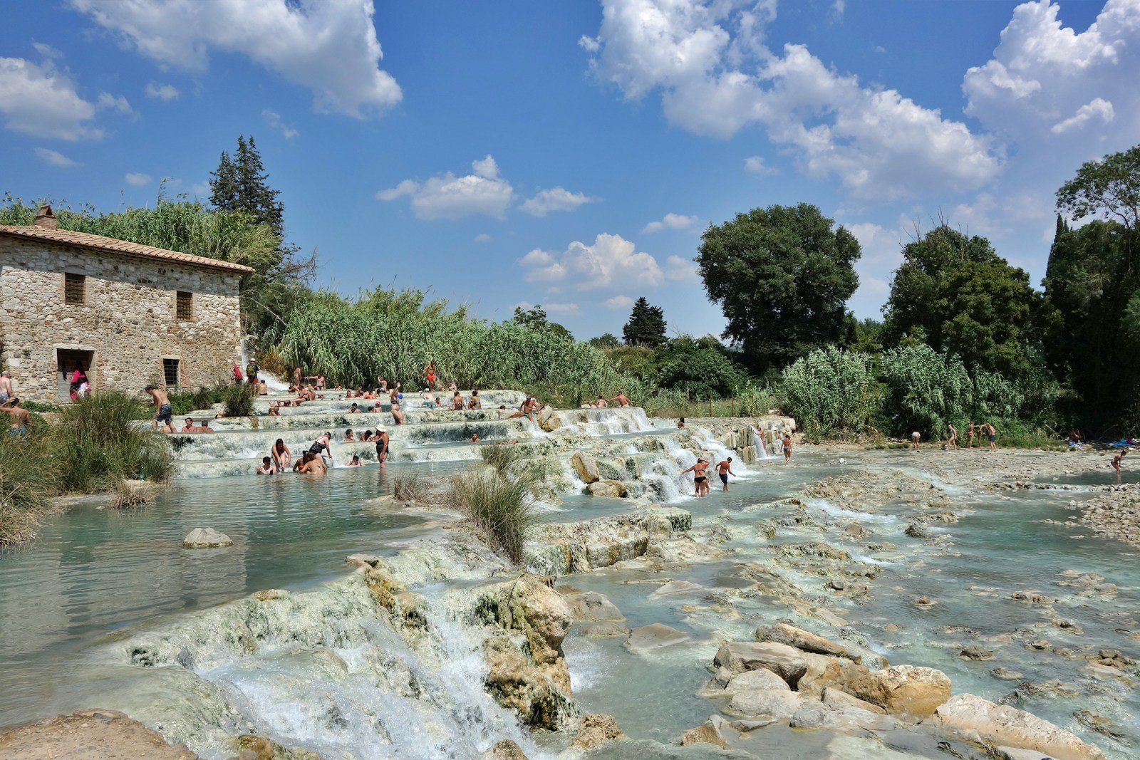 a group of people swimming in a river next to a stone building