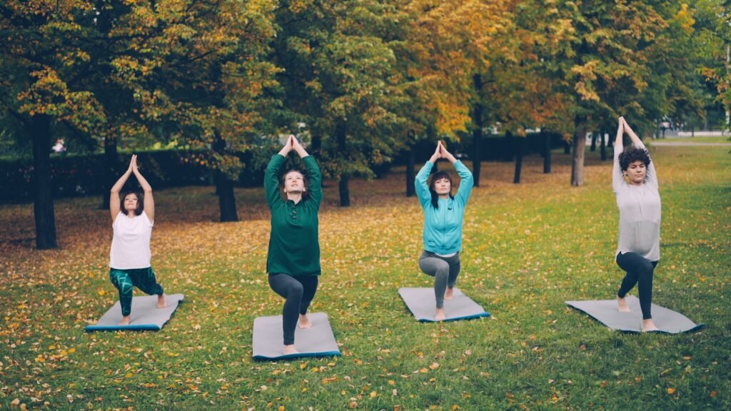 Four women practicing yoga in a park during autumn.