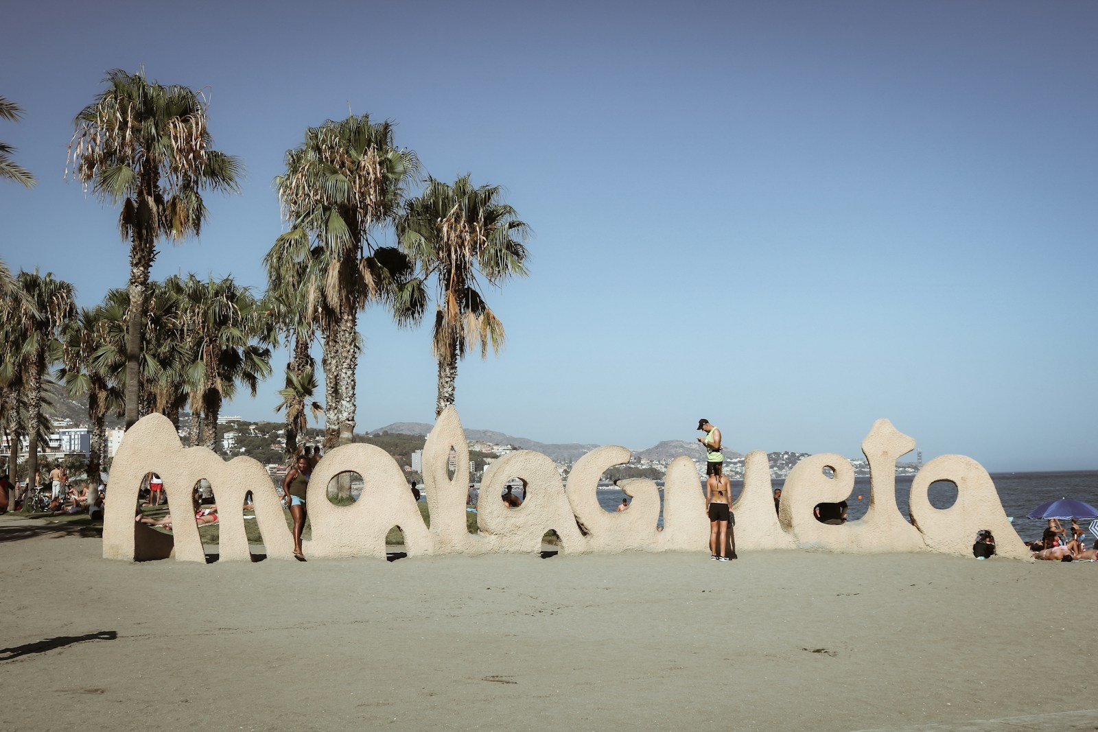 Large letters spell out malaga on a sandy beach.