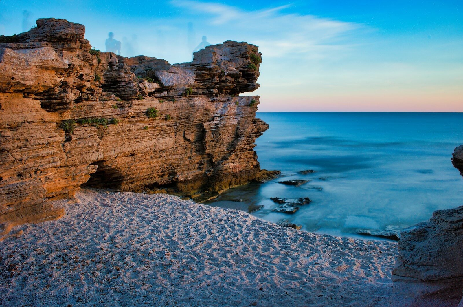 Rocky cliffs meet a sandy beach at dusk.