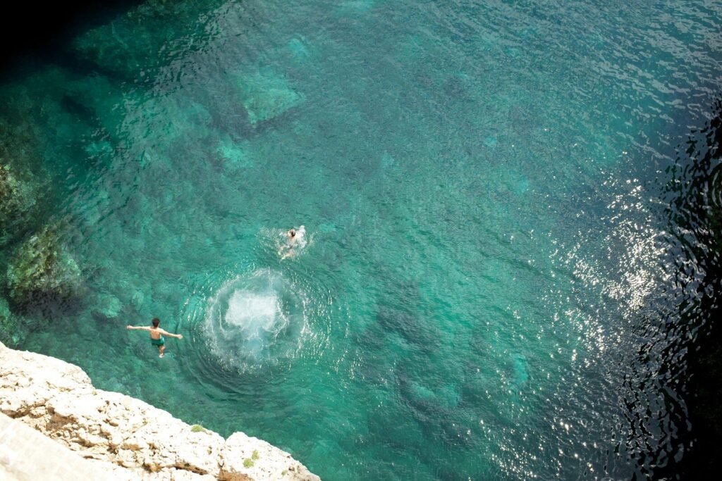 two people swimming in the water near a cliff