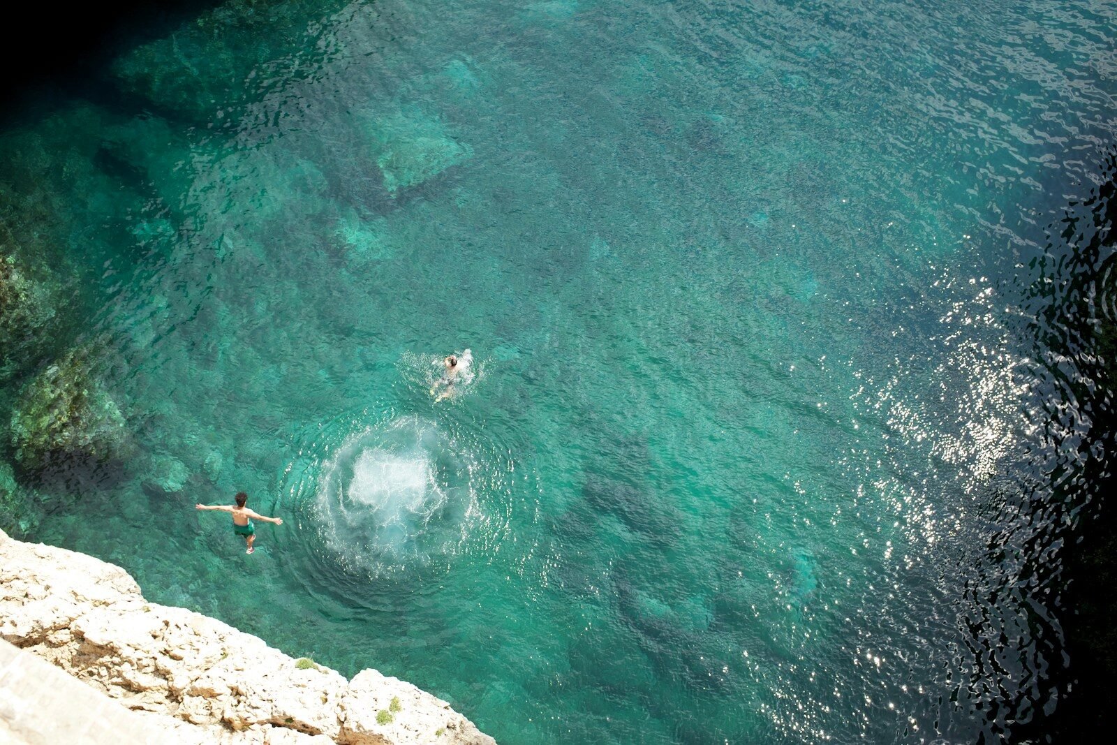 two people swimming in the water near a cliff